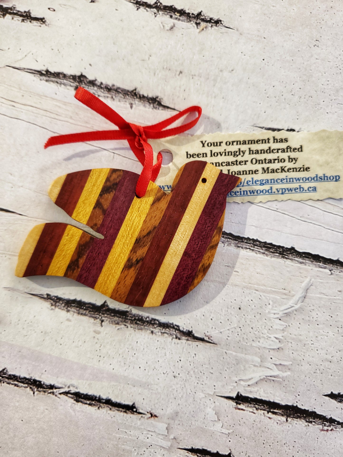 One wooden dove ornament with red and yellow coloured wood stripes, on a birch paper background.