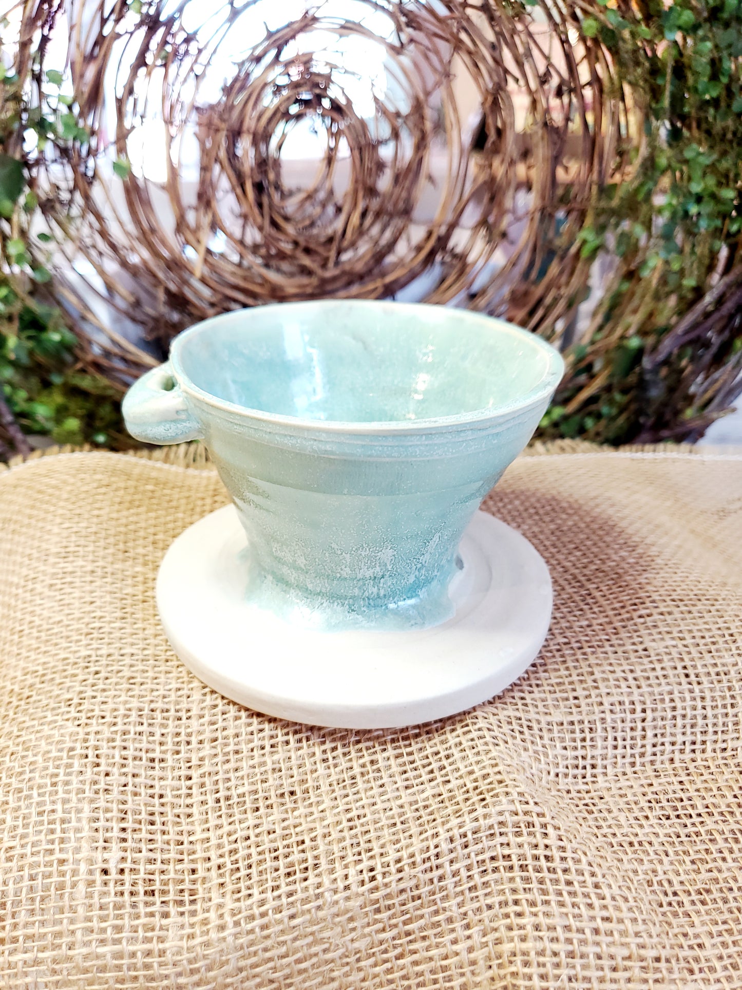 Back of a teal ceramic pour over cup with a gold butterfly on it, against a vine background
