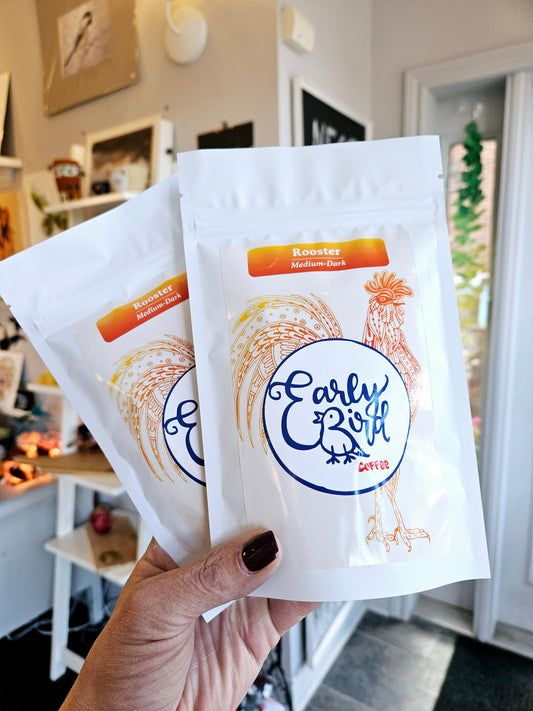 Hand holding two packs of Early Bird coffee beans