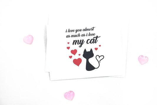 A greeting card reads I love you almost as much as i love my cat on a white background with hearts